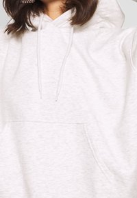 Hellgrauer, strukturierter Hoodie mit einer Vordertasche, Kordelzügen und einer lockeren Passform. Er besteht aus einem weichen, fleeceähnlichen Material und hat dezente Nahtdetails.