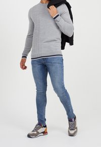 Szary sweter dzianinowy z teksturowanym przodem, prążkowanymi mankietami i dołem. Połączony z niebieskimi rurkowymi dżinsami i wielokolorowymi trampkami. Czarna kurtka zarzucona na ramię.