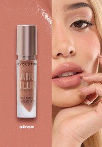 Mjuk, matt vätske-läppprodukt i genomskinlig förpackning med en metallisk lock, som har en varm nudefärg märkt "siren." Närbild av läpparna visar en slät yta.