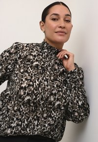 Blusa nera e beige con motivo, colletto alto, maniche a sbuffo e texture arricciata. Presenta un tessuto morbido e leggero.