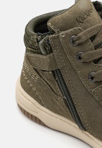 Botín de ante verde con un collar acolchado, cordones en el frente, cremallera lateral, acentos texturizados y una suela de goma beige con patrones de agarre.