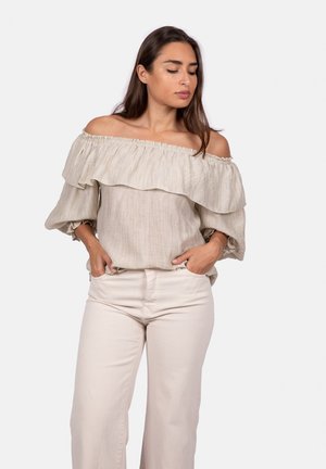 Beige off-the-shoulder blouse van textuurstof, met ruches en wijdvallende mouwen. Gecombineerd met lichtbeige wijde broek.