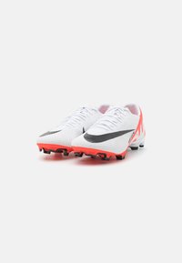 Scarpe da calcio bianche con superficie texturizzata, logo swoosh nero e vivaci accenti rosa sul tallone. Tacchetti neri resistenti per una buona trazione.