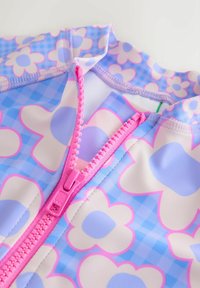 Mitmevärviline ujumisriietus, millel on sinine ruuduline muster suurte valgete lilledega. Sellel on roosa lukukinnitus ja sile kangastekstuuri.