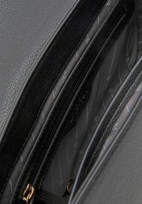 Interior de bolsa de cuero negro con textura suave; cuenta con un bolsillo con cremallera y un forro estampado en tonos de gris.