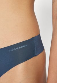 Dunkelblaues Bikini-Höschen mit glatter Textur, elastischem Bund und subtiler Logo-Prägung an der Seite. Nahtloses Design erhöht den Komfort.