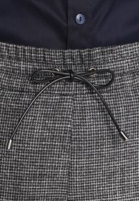 Zwart-witte houndstooth-gepatroneerde broek met een trekkoord taille, zilveren hardwareaccenten en een gladde, gestructureerde afwerking.