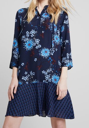 Robe florale marine avec des fleurs bleues et de petits pois blancs. Jupe évasée avec un motif en cercles bleus. Encolure boutonnée et manches trois-quarts.