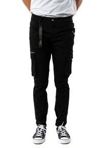 Pantalones cargo negros con varios bolsillos, un corte ajustado y una etiqueta con el logo en la cinturilla. Combinados con zapatillas bajas blancas y negras.