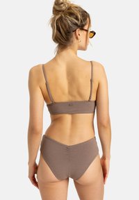 Bikini texturé marron avec bretelles réglables. Le haut présente un design de bande simple, tandis que le bas a une taille haute et une couverture minimale.