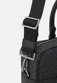 Sac noir en synthétique avec un motif texturé, doté d'une fermeture éclair en métal argenté et d'une sangle noire réglable avec une boucle en métal.