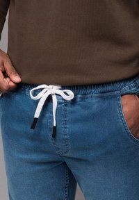 Jasnoniebieskie spodnie dresowe z elastycznym pasem, z białym sznurkiem ściągającym zawiązanym w kokardkę oraz czarnymi plastikowymi końcówkami. Gładka tekstura jeansu.