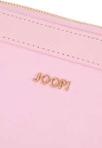 Różowy portfel na suwak z teksturowanego materiału, zdobiony złotym logo "JOOP!", z wytłoczonymi wzorami i przeszyciami wzdłuż brzegów.