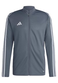 Veste de sport gris foncé avec un design à trois rayures blanches sur les manches, fermeture éclair sur le devant et logo de la marque blanc sur la poitrine.
