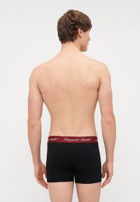 Boxer-briefs noirs avec une ceinture élastique bordeaux portant le texte "Originals Studio". Texture lisse, ajusté, avec un design de coupe standard.