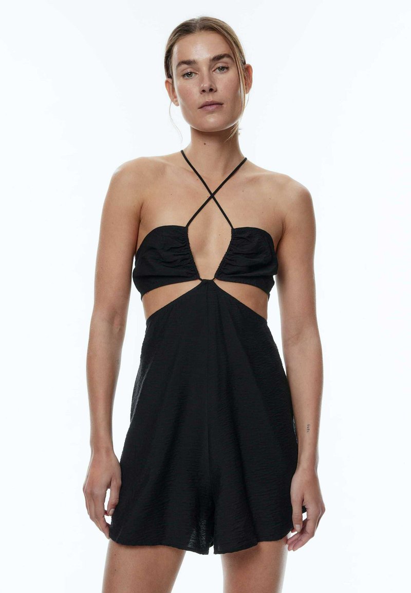 Schwarzer Jumpsuit mit Halterneck, strukturiertem Stoff, ausgeschnittenen Seitenteilen und tiefem V-Ausschnitt. Dünne Kreuzträger im Rücken.