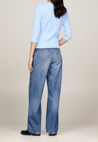 Top fitted di un blu chiaro con maniche 3/4 abbinato a jeans in denim blu a vita alta, larghi. Tessuto testurizzato e design semplice, senza motivi visibili.