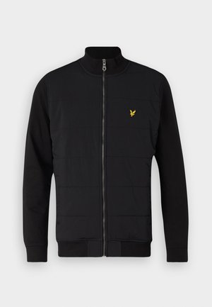 Giacca nera con zip frontale, caratterizzata da un design trapuntato sul corpo, maniche lunghe lisce e un piccolo logo giallo sul petto.