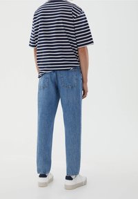  Marinblå och vit randig kortärmad skjorta i kombination med ljusblå raka jeans och vita sneakers med marinblå detaljer, sedd bakifrån.