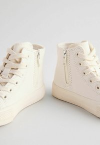 Sneakers alte in tela bianca con lacci e cerniere laterali, caratterizzate da una superficie liscia e suole rotonde in gomma.