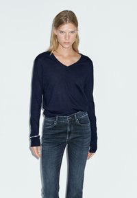 Marineblauwe V-halstrui van zachte stof met lange mouwen, gecombineerd met donkerblauwe jeans met een klassiek vijf-pocket ontwerp.