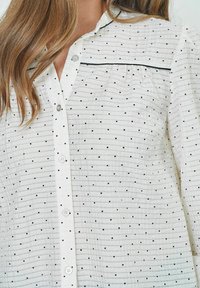 White button-up shirt featuring black polka dots and horizontal stripes, with a small collar and slightly puffed sleeves.