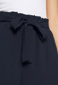 Navy blue waist trousers with a gathered elastic band and a tied bow detail, made from soft fabric with a smooth texture.