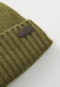 Olive roheline ribadega kudumise beanie, mille nööbivardasse on õmmeldud pruun ristkülikukujuline nahk Barbour England logo patch.