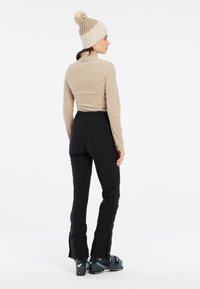 Maglia beige a maniche lunghe come primo strato, pantaloni neri aderenti con zip alle caviglie e un cappello lavorato a maglia beige con pon-pon sulla sommità.