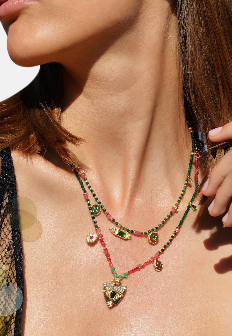 Collier en couches avec des accents dorés, des perles vertes et roses, différentes formes de breloques, avec un motif texturé et des détails complexes.