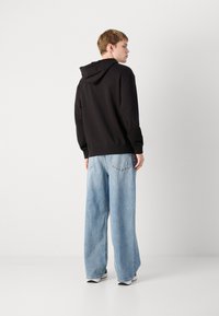 Svart hettegenser med en avslappet passform, sammen med lyseblå vide jeans. Antrekket har et uformelt og komfortabelt design.