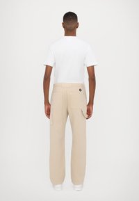 Pantalones cargo beige con bolsillos laterales y un corte relajado, combinados con una camiseta blanca. Diseño sencillo con detalles mínimos.