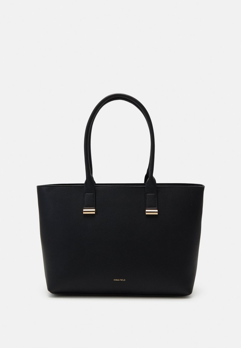 Sac cabas en cuir noir avec deux anses et des détails en métal doré, présentant une surface texturée et un petit logo près de la base.