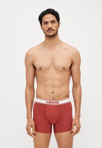 Crvene pamučne bokserice s bijelim pojasom na kojem se nalazi "Levi's" logo. Prilagođen dizajn s glatkom teksturom i elastičnim pojasom.