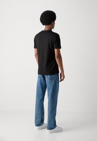 Camiseta negra de manga corta con una textura suave, combinada con unos vaqueros holgados de color azul claro y zapatillas blancas. Diseño simple, sin patrones visibles.