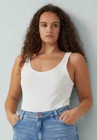 Wit katoenen tanktop met brede bandjes, ronde halslijn, gladde textuur, gecombineerd met lichtblauwe high-waisted denim jeans en minimale accenten.