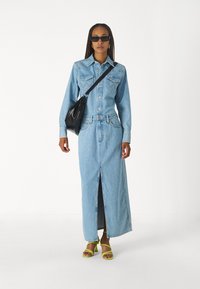 Világoskék farmering és szoknya, elöl hasítékkal, fekete keresztpántos táskával és élénk sárga magassarkú szandállal párosítva. Négyzet alakú napszemüveg viselve.