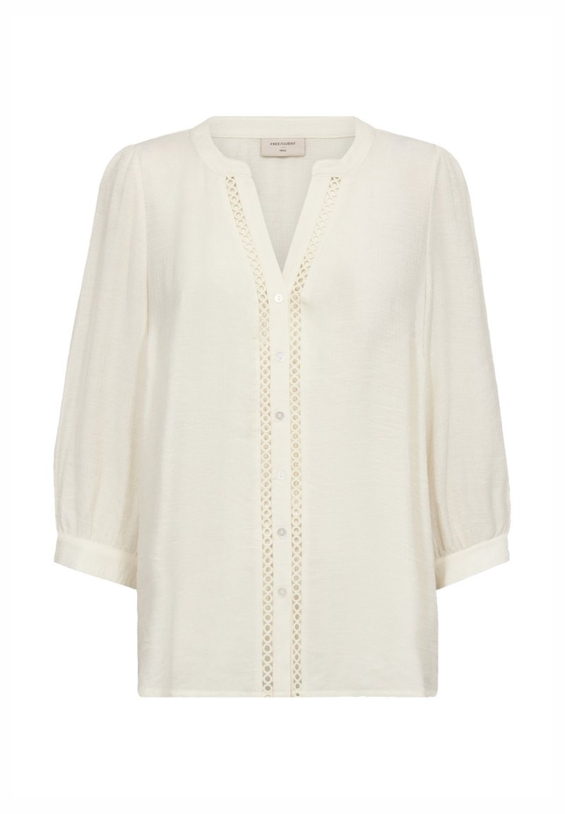 Blouse blanche à manches longues avec encolure ronde, ouverture boutonnée sur le devant et bordure ajourée décorative le long de la patte de boutonnage.