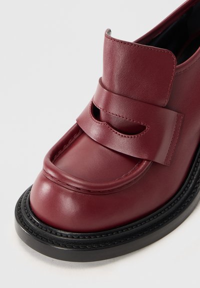 Burgundské kožené mokasíny s širokým páskem a výřezem, čtveratou špičkou a tlustou černou podrážkou, vyfotografované na bílém pozadí.