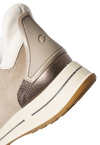Sneaker featuring a beige suede body, white leather accents, and a shiny brown heel. Rubber sole with contrasting black and beige stripes.