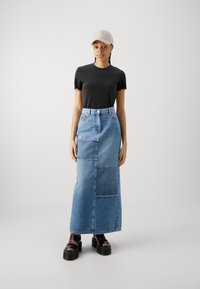 Gonna maxi in denim con design a patchwork, colore azzurro chiaro, vita alta e bordi sfilacciati, abbinata a una maglietta nera a collo rotondo e stivali chunky.