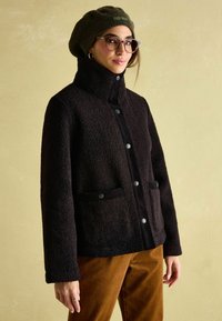 Czarna, fakturowana kurtka polarowa z wysokim kołnierzem, zapięciem na guziki i akcentami z korduroju. Posiada dwie przednie kieszenie.