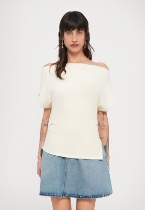 Off-white short-sleeve top with an asymmetrical off-shoulder design, paired with a light blue denim skirt featuring a frayed hem.
