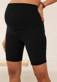 Shorts de maternité noirs avec une taille élastique haute et une texture lisse, conçus pour le confort et la flexibilité pendant le port.