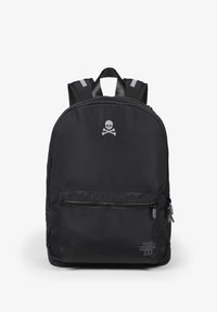 Mochila negra de nailon con un bolsillo frontal con cremallera, acentos reflectantes en las correas y un logo de calavera plateado en la parte frontal. Textura suave.