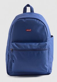Modrý batoh z nylonu. Má přední kapsu na zip, horní rukojeť a boční síťovanou kapsu. Červené logo Levi's na přední straně.