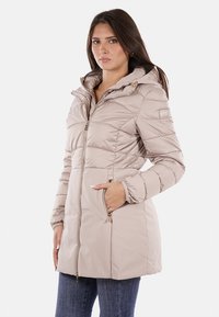 Giacca puffer beige chiaro con cappuccio, chiusura a zip frontale, tasche laterali e cuciture diagonali. Presenta una texture liscia e dettagli in metallo dorato.