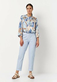 Lichtblauwe blouse met een bloemenpatroon, gecombineerd met lichtblauwe op maat gemaakte broeken en beige sandalen. De outfit heeft een relaxte pasvorm en een zachte textuur.