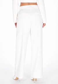 Pantaloni evazați albi, cu o textură netedă, având talie medie, buzunare pe spate și detalii de cusătură subtile.