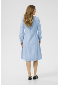 Svetlomodré denimové šaty s dlhými rukávmi, s dĺžkou po kolená a zhromaždenými detailmi na ramenách. Obsahujú gombíkové zapínanie na zápästiach.